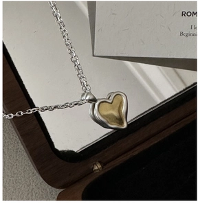 Close-up of two-tone matte 925 silver and gold heart pendant on an elegant wooden jewelry box
