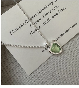 Vue macro d'un collier cœur en argent avec pierre verte sur une carte de poésie