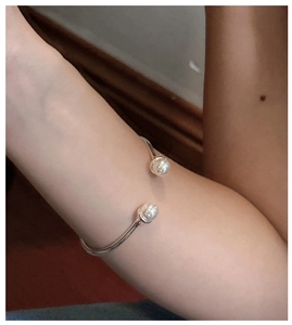 Close-up of a silver S925 open bangle featuring two elegant white pearls on a female wrist