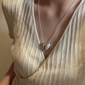 Polished S925 silver heart pendant necklace with sleek snake chain on knitwear