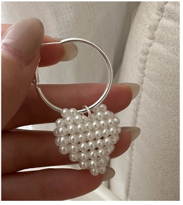 Gros plan d'un pendentif cœur en perles tressées sur un anneau en argent tenu à la main