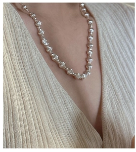 Detail of silver beaded necklace with polished spheres worn over beige knit sweater