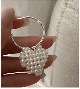 Détail de créoles argentées avec pendentif en forme de cœur en perles blanches