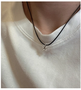 Dettaglio di un ciondolo a stella marina in argento su cordino nero indossato su t-shirt