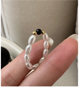 Dettaglio anello di perle bianche con accenti dorati indossato su un dito