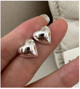 Close-up of hand holding minimalist 3D heart-shaped sterling silver stud earrings