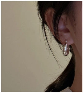 Detailed view of silver hoop earrings with spiral shell texture worn by a model
