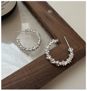 Macro detail of silver C-shape hoop earrings with irregular twisted metal texture