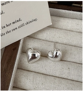 Macro view of polished S925 sterling silver heart studs in a beige textured jewelry box