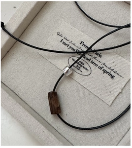 Close-up of S925 sterling silver bead and dark wood cylinder on a black woven cord necklace