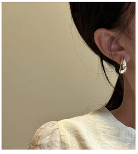Close-up of chunky silver crescent hoop earrings on model with high-shine metallic finish