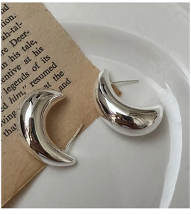 Detailed view of polished S925 sterling silver crescent earrings on vintage paper