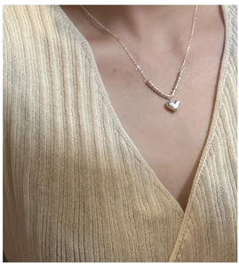 Close-up of minimalist S925 sterling silver heart necklace worn with V-neck knitwear