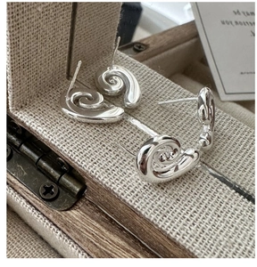 Macro shot of silver conch-shaped stud earrings in a vintage linen jewelry box