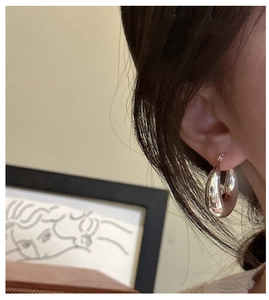 Close-up of a model wearing large polished S925 sterling silver hollow hoop earrings
