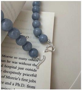 Detail view of a gray-blue bead necklace with a silver OT toggle clasp on a book