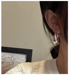 Close-up of a high-polished silver teardrop earring on a model wearing a white sweater