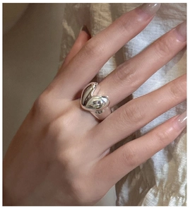 Close-up of polished S925 sterling silver heart ring worn on hand with soft fabric background