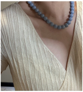 Detail view of a round blue bead necklace worn by a model in a minimal soft knit sweater