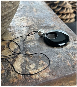Macro view of a minimalist 50mm black obsidian donut pendant on a natural rock surface