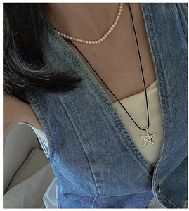 Close-up of a silver starfish pendant layered with a white bead necklace on denim