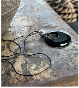 Macro shot of minimalist obsidian round pendant with silver bead on textured rock surface
