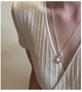 Close-up of a minimalist silver O-chain necklace featuring an irregular oval pendant on a model