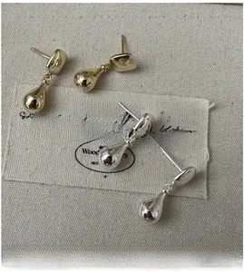 Macro shot of minimalist teardrop earrings in polished gold and silver on linen