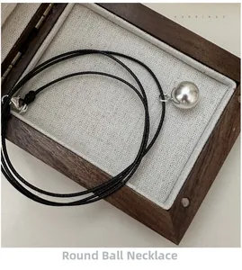 Detailed view of polished silver sphere pendant on minimalist black cord necklace in wood box