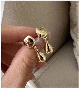 Close-up of gold water drop earrings featuring polished geometric shapes on soft fabric