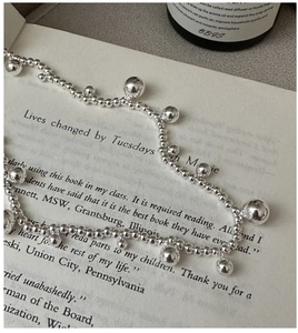 Detail shot of a silver beaded necklace with dangling spheres resting on a book