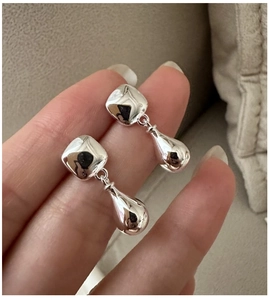 Detail of silver drop earrings with mirror finish held in hand against neutral background