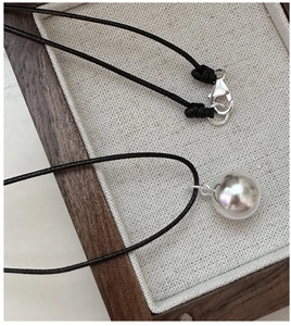 Macro detail of S925 sterling silver ball pendant with black rope chain on linen texture