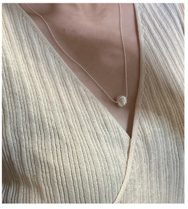Detail of silver S925 necklace with fluid texture bead pendant on neck with knitwear