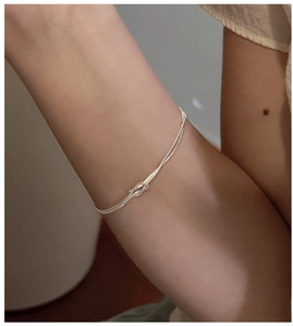 Nahaufnahme eines minimalistischen S925 Silber-Doppelknotenarmbands am Handgelenk