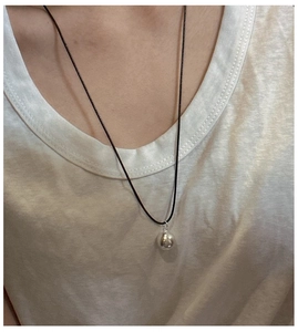 Close-up of minimalist silver sphere pendant on a thin black cord worn by a model