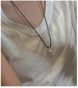 Detail of minimalist S925 silver ball pendant on a black cord necklace worn by a model