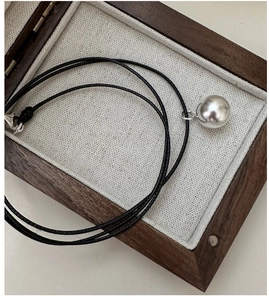 Macro detail of a large polished silver ball pendant on a black cord necklace in a gift box