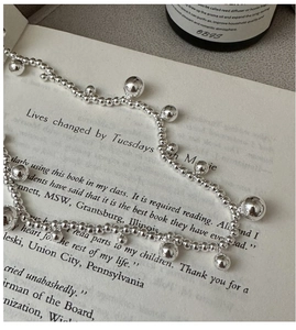 Detail of S925 sterling silver beaded necklace over an open book and perfume