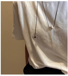 Minimalist textured silver bead pendant on thin black cord worn over white shirt