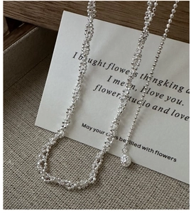 Gros plan d'un collier de perles argentées texturées scintillantes sur carte blanche