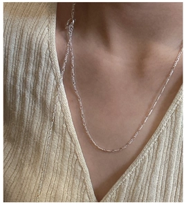 Detail of silver Figaro chain necklace showing the polished oval links on a beige sweater