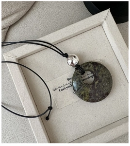 Détail du pendentif rond en pierre naturelle verte avec perle argentée et cordon noir
