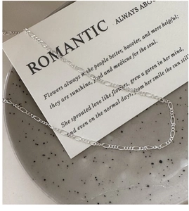 Detailed close-up of a silver Figaro chain necklace with polished long and short links