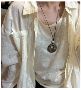 Détail d'un pendentif en pierre vintage sur cordon noir sur chemise en lin blanc