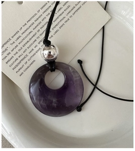 Macro view of purple amethyst stone pendant with silver bead on black cord necklace