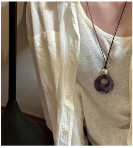 Macro view of purple amethyst ring pendant with silver bead on a black cord necklace