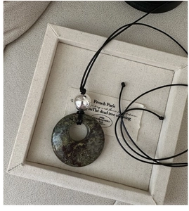 Détail d'un pendentif rond en pierre naturelle vert foncé avec perle argentée sur cordon