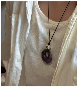 Close-up of a minimalist purple natural stone ring pendant on a black cord necklace