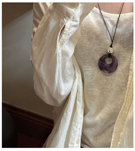 Detail of natural purple stone ring pendant with silver bead on black woven cord